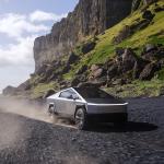 Tesla cybertruck driving on rocky beach with cliffs in background.