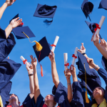 Students at a high school graduation holding diplomas and throwing graduation caps.