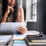A woman seated at a desk considering investment options on a tablet.