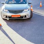 A young female student driver is being taught how to go around traffic cones.