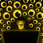 Photo illustration of student at laptop surrounded by many pairs of googly eyes watching; surveillance concept.