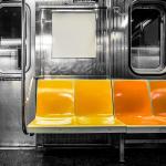 A black and white photograph inside a subway train but the seats are colored in yellow and orange.