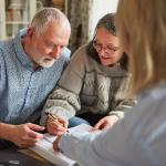 An elderly couple signing documents with a legal professional.