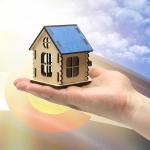 An illustrated concept of financial support for housing, with hands holding a model of a wooden house against the background of the flag of state of Colorado.