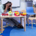 Teachers sitting in a young student classroom with head in her hands.
