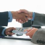 A client and car dealer shake hands after agreeing to a sales contract.