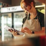 A small grocery owner using a digital tablet in her store.