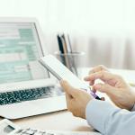 Businessman looking through phone and with a laptop is filling out a tax return form.