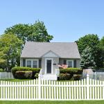 White picket fence in front of small bungalow house.