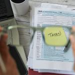 A selective focus of person holding eyeglasses over a tax form and the word "taxes" on a note.