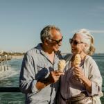Smiling senior couple with ice cream cones standing near the beach in California.