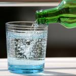 Sparkling water poured onto a glass from its bottle.