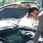 A car owner inspects his car's hood after it breaks down.