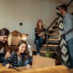 Four people who are co-living in a house are unpacking boxes of home items.