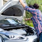 A female car owner opening the hood of her silver car to inspect its engine.