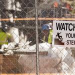A 'watch your step' warning sign on the fence of a construction site.