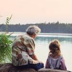 Grandparent sits with grandchild, overlooking the river on a warm day.