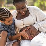 A black mother and her son touching her pregnant belly doing heart shape with hands.