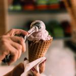 Worker scooping ice cream into waffle cone.