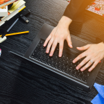 An overhead view of a student typing on a laptop surrounded by school supplies.