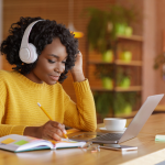 A teenager studying online wearing a headset, taking notes.