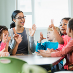 A young teacher sitting with her students at a table. 