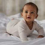 A baby lying on their stomach on a white bed.