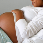 A pregnant person lying in a hospital bed cradling her stomach.