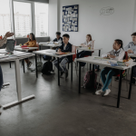Students looking at a teacher in front of them in a classroom.  