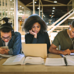 Three college students fixated on their laptops and smartphones.