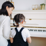 A woman and a little girl sit at a piano.