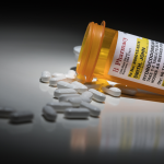 A prescription bottle for Hydrocodone on its side with pills spilling out.