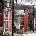A row of brick houses with messy front yards and power lines in front of the buildings.