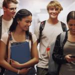 A group of four young students walking together in a hallway, likely in a school all smiling and engaged with each other.
