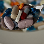 A spoon filled with a variety of colorful pills and capsules of different sizes and shapes.