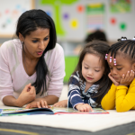 A teacher reading to two toddlers in a classroom.