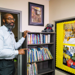A teacher speaking in his classroom, pointing to posters featuring Black history icons figures and Cesar Chavez. 