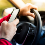 Driver with one hand on the steering wheel and one hand texting.