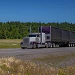 A large semi-truck driving along a highway in a rural area.
