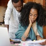 A young Black couple looking concerned while looking at their bills.