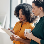 Two women look at a tablet in a bright office.
