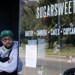 Business owner leaning against the wall outside at his Sugarsweet Cake and Cookie Studio.