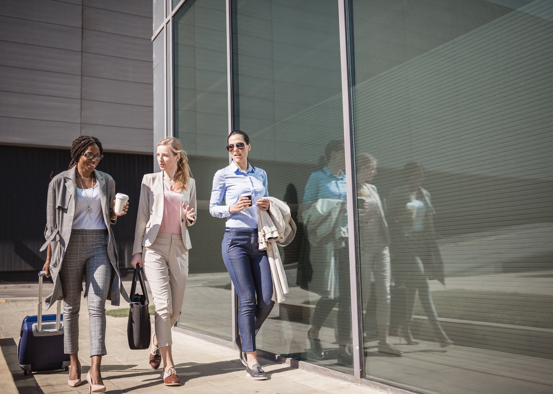Three business women walking down the street, one pulling a rolling bag.