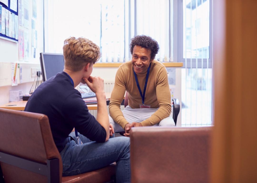 A counselor leans in and smiles to talk to a student in his office.