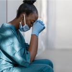 Female health care worker crouched on the floor with head in hands.