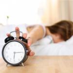 Woman hitting alarm from bed.