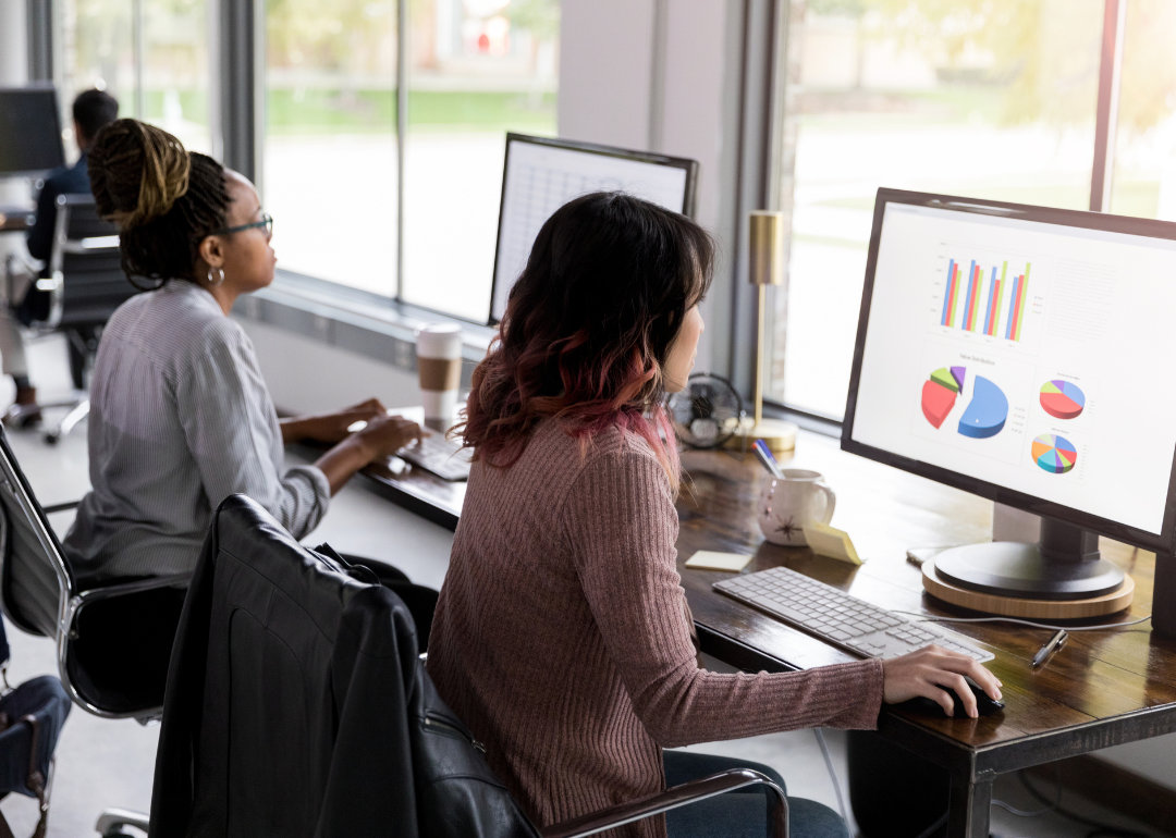 Two women doing research analysis on desktop computers.