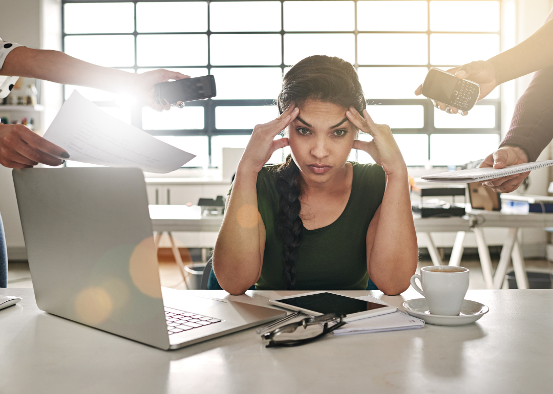 A stressed woman at a desk with hands coming at her from all sides with phones and tasks.
