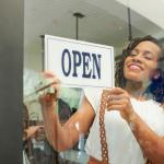 Young woman turning around the open sign on her shop's door.