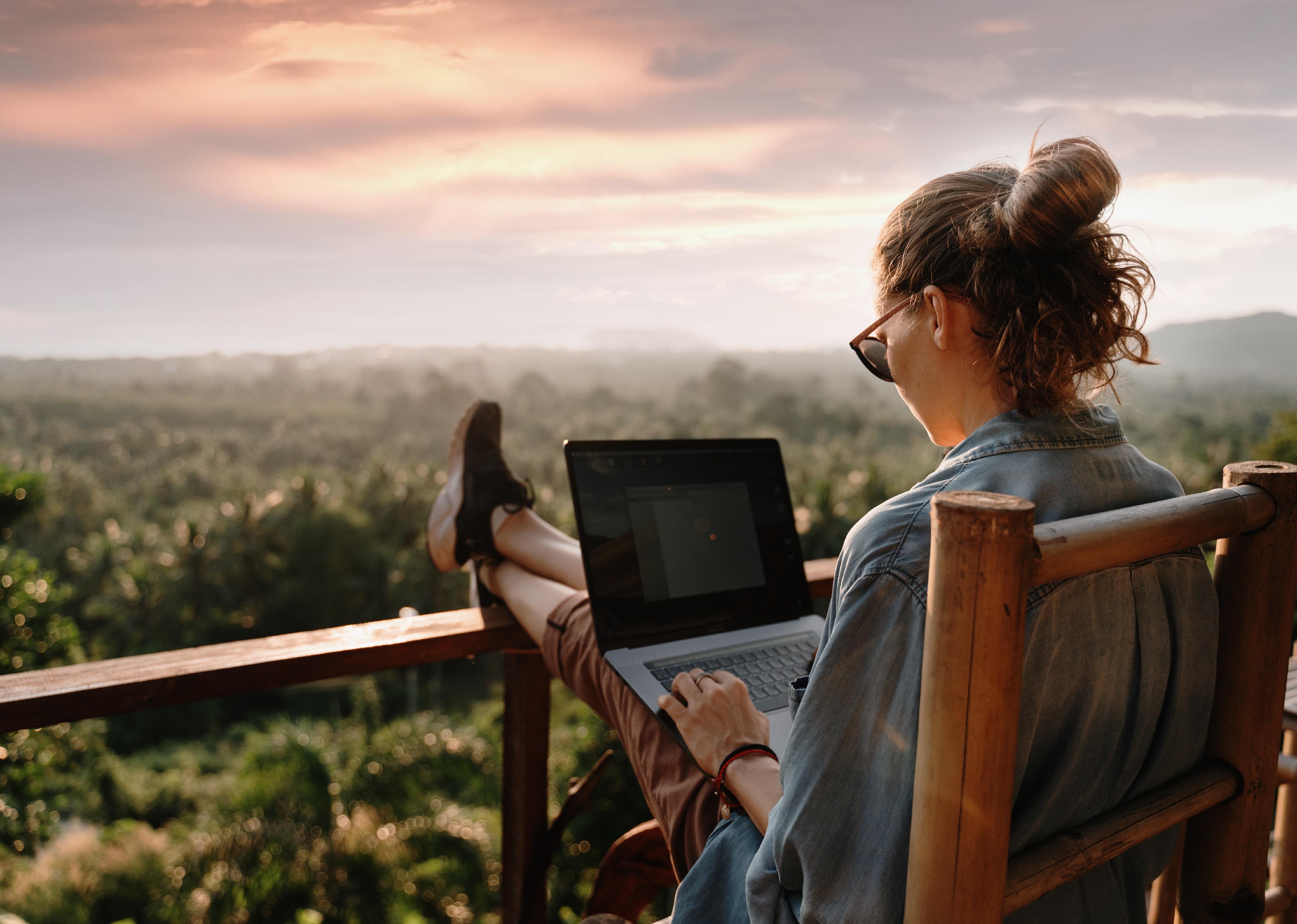 Young person working on their laptop while sitting on a deck.